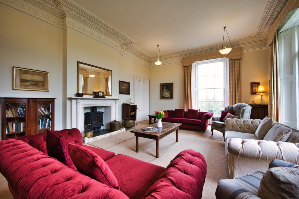 large red and cream sofas in stately drawing room with ornate fireplace